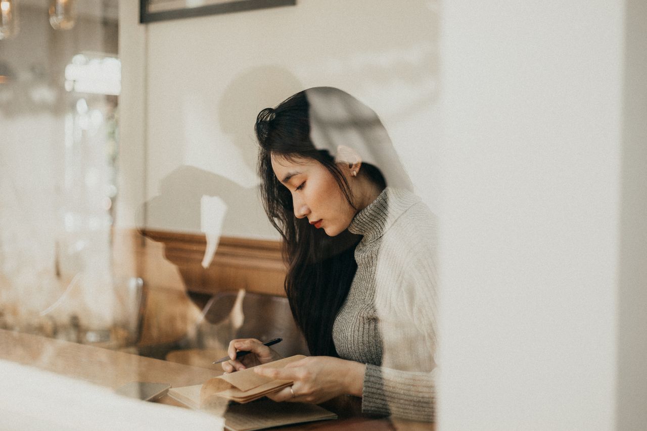 Asian woman writing in notebook in cozy cafe setting