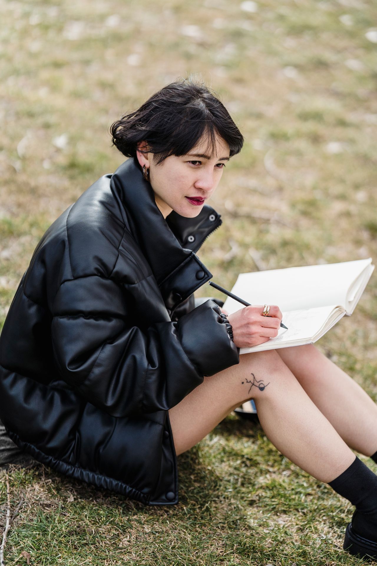 Asian female student writing seriously on grassy lawn